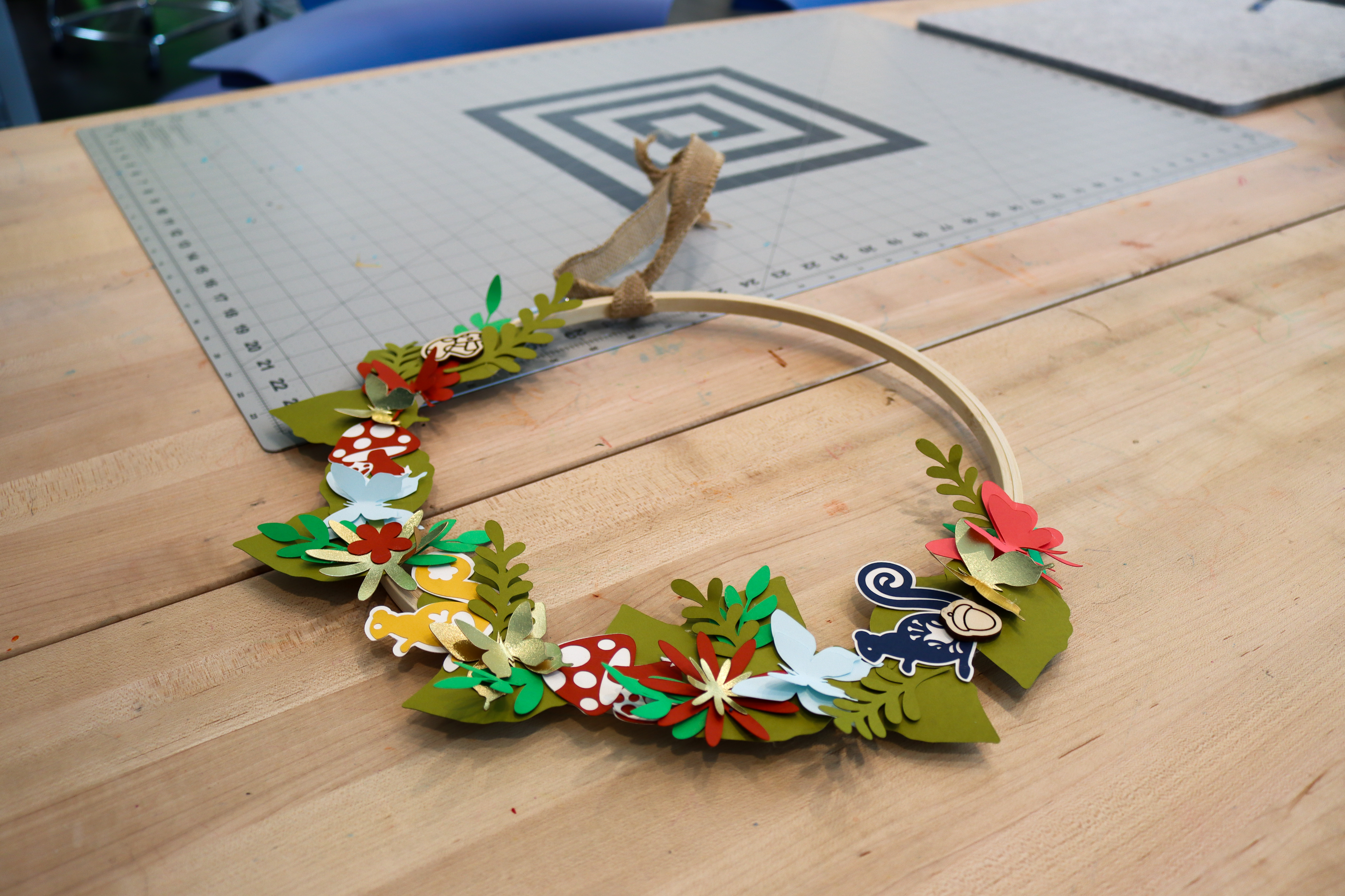 Wreath on a table in Studio 411 made from an embroidery hoop and paper cut-out shapes of leaves, butterflies, mushrooms, and squirrels.