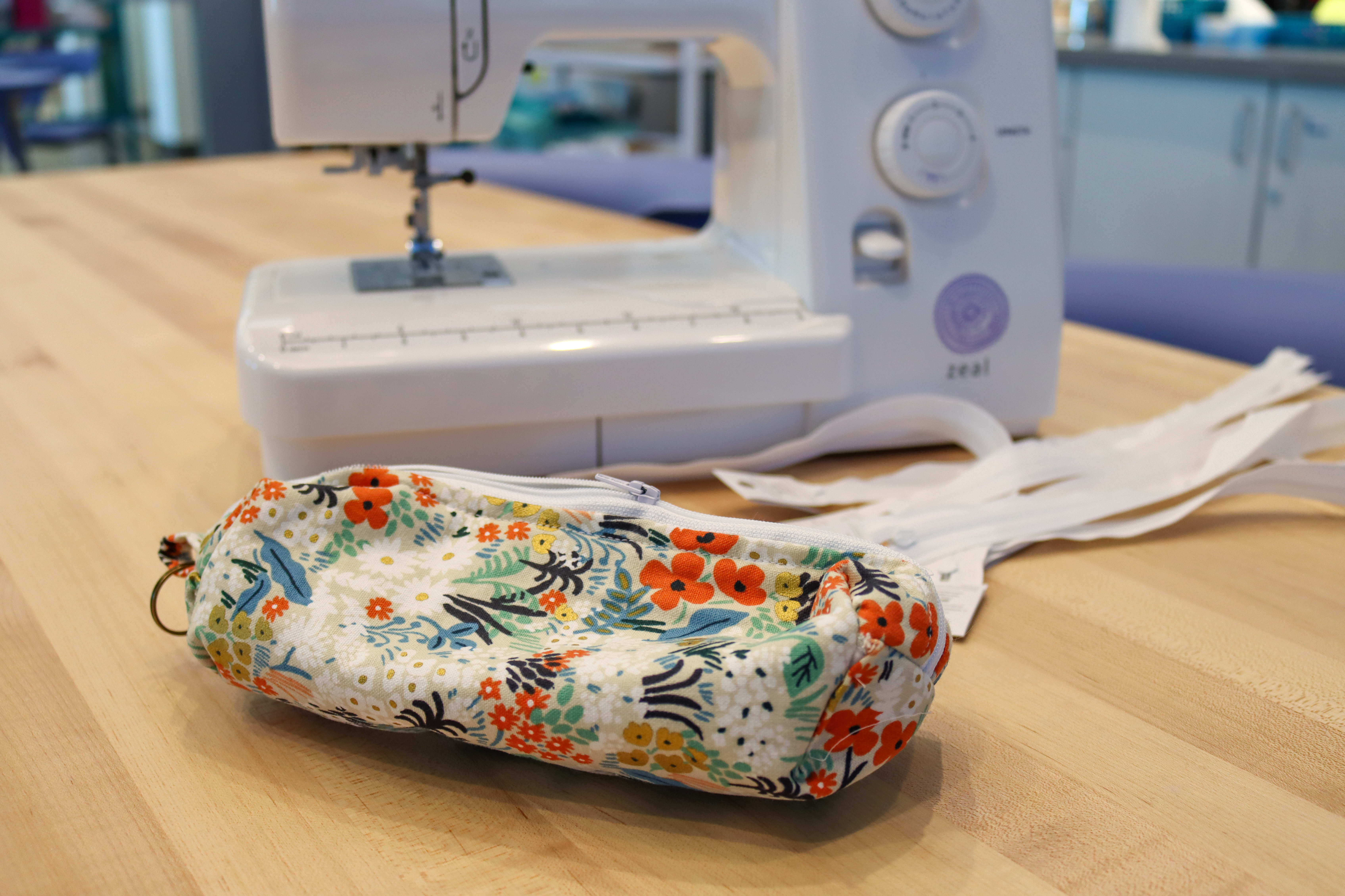 Floral-patterned pencil pouch made of fabric on a table with a sewing machine in the background.