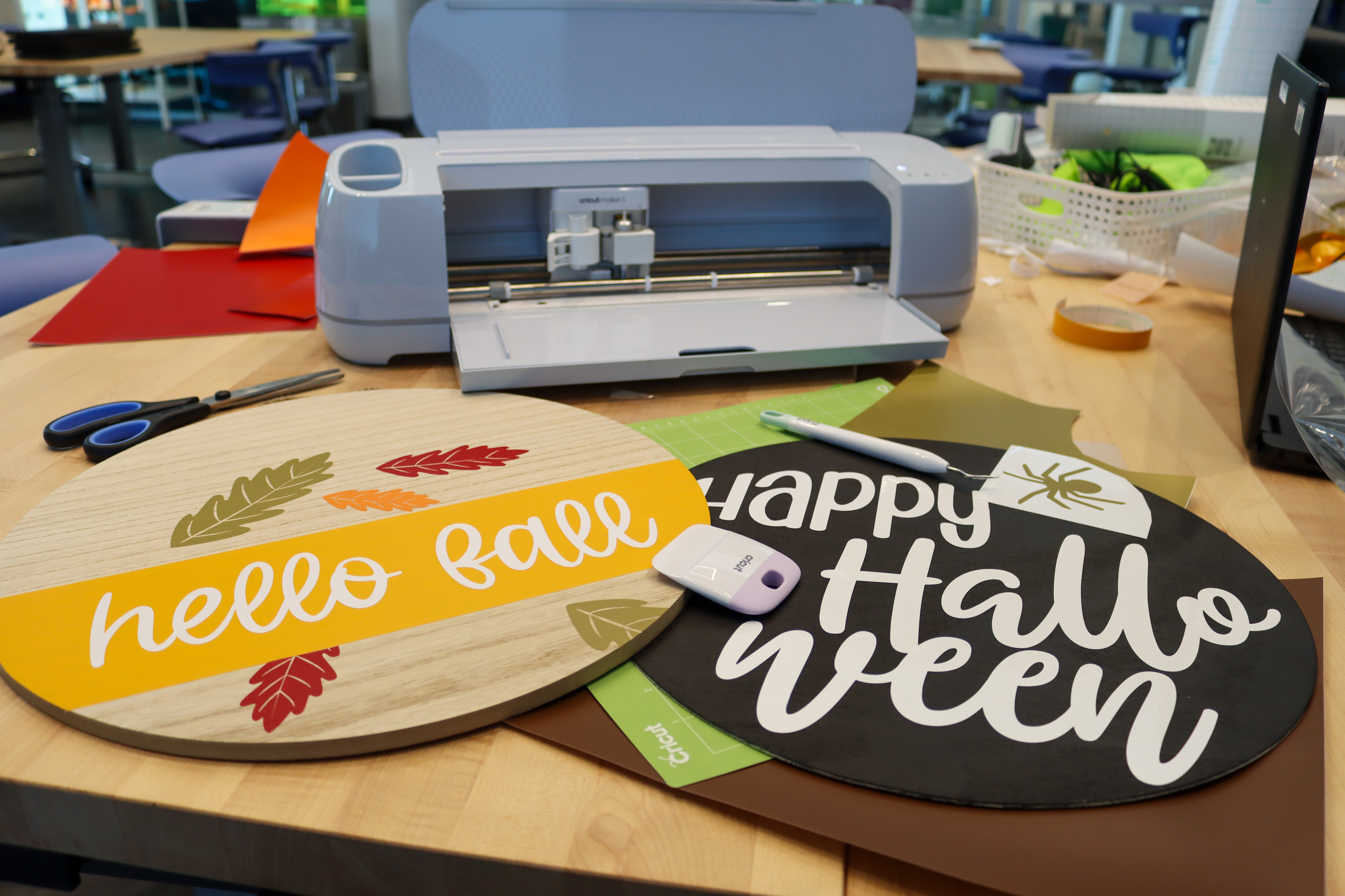 Two circular wooden signs on a table in Studio 411. One says hello fall with red and orange leaves on it and the other is black and says Happy Halloween. 