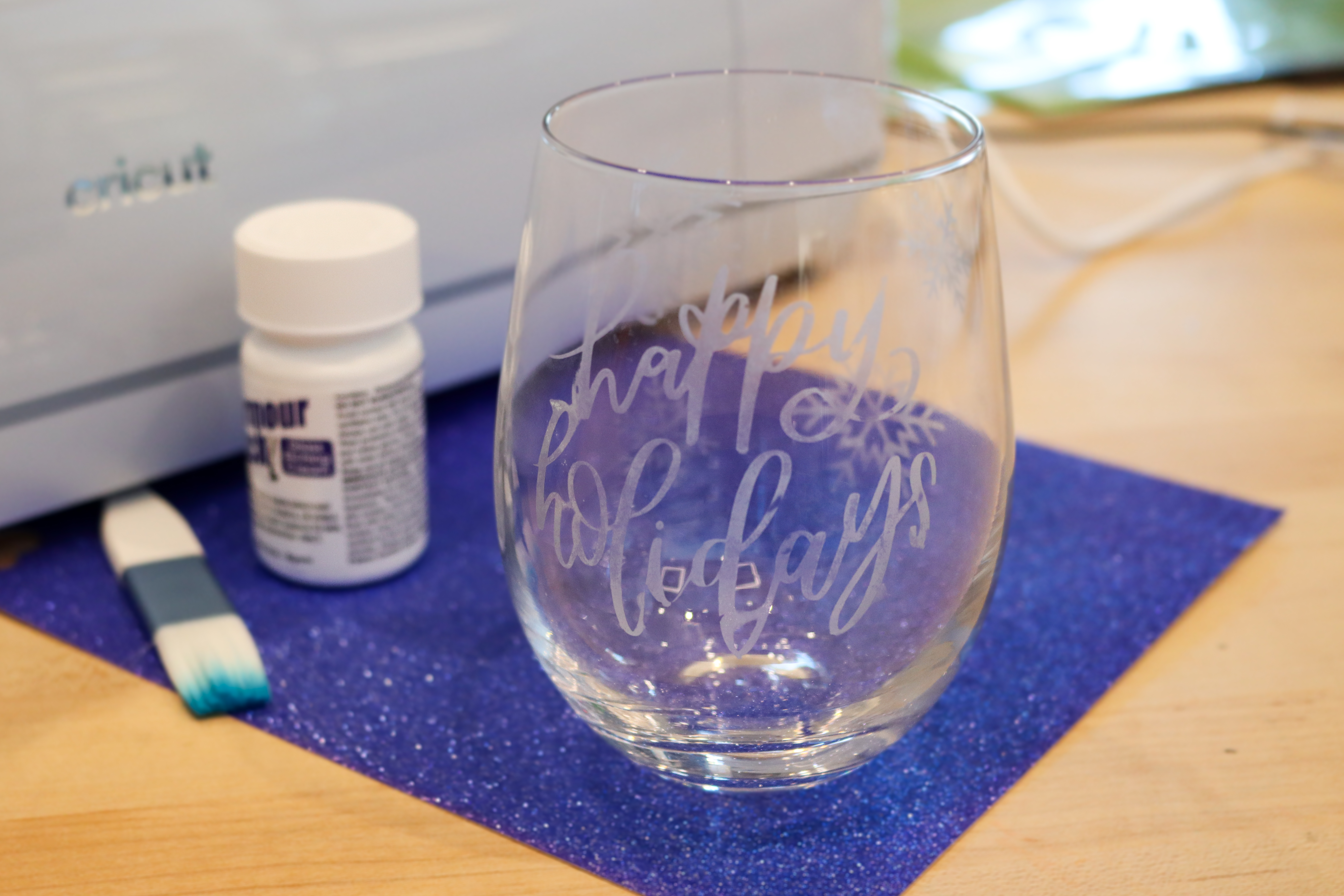 Stemless wine glass on a table with the words Happy Holidays etched onto it in a script font