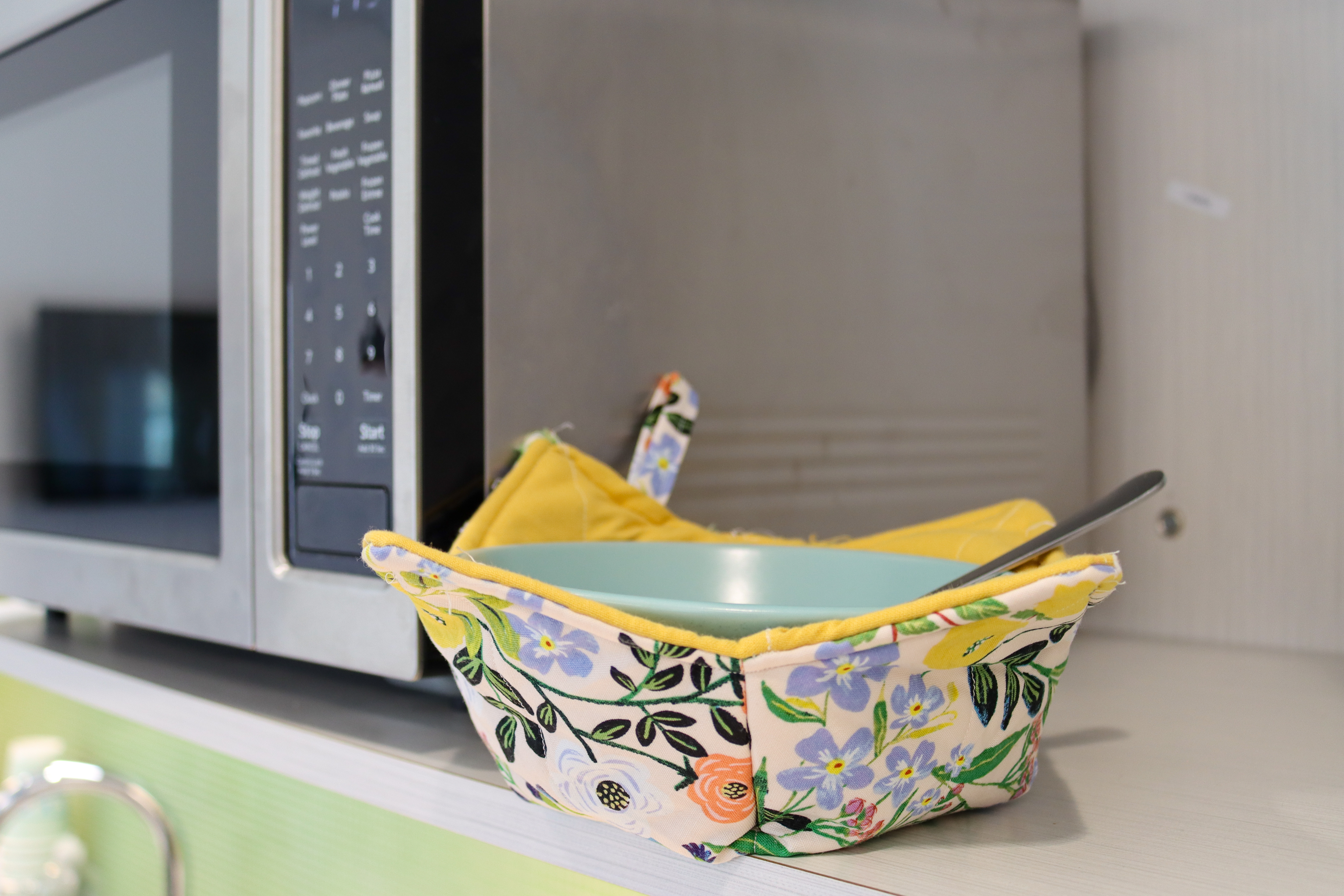 Bowl in a floral cotton bowl cozy next to a microwave on a counter